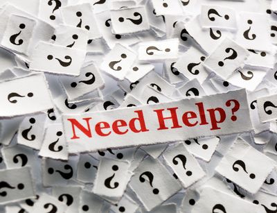 Viele Papierschnipsel mit Fragezeichen und dazwischen auf einem Zettel in roter Schrift: "Need Help?".