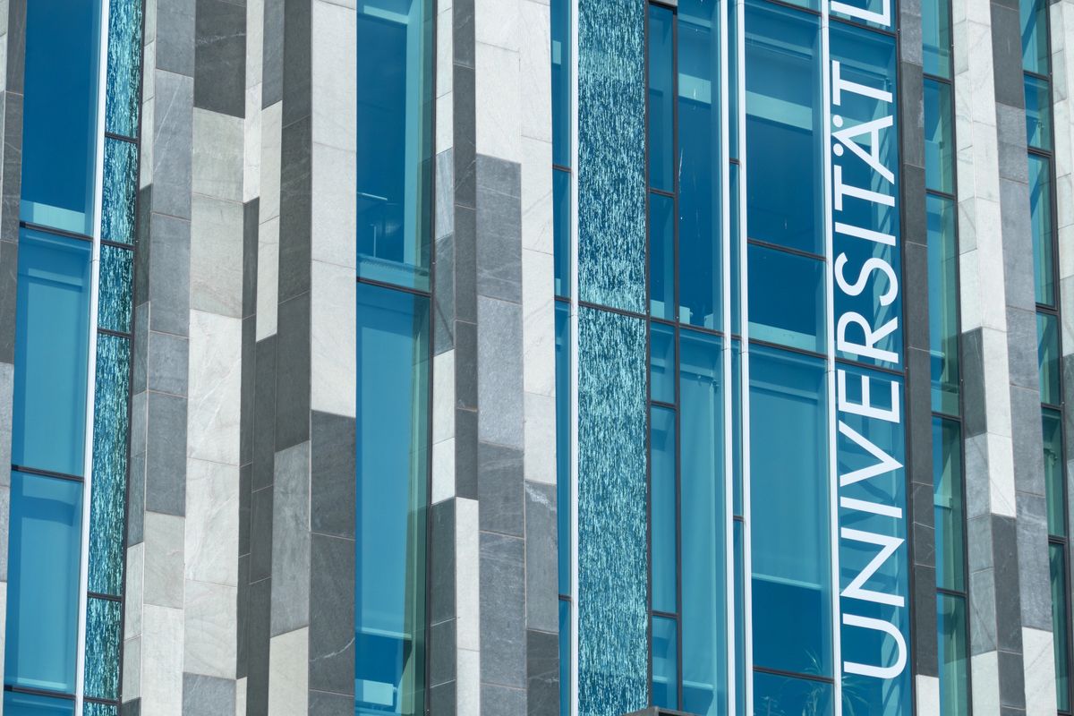 zur Vergrößerungsansicht des Bildes: Glasfassade des Augusteums der Universität Leipzig, vertikal ist der Schriftzug „Universität” zu erkennen.