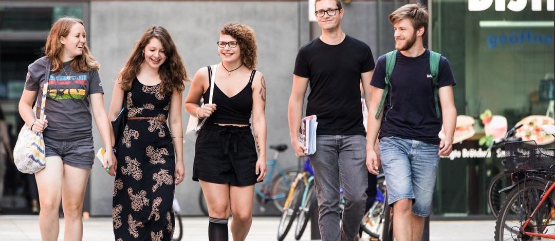 Studierende gehen nebeneinander auf dem Campusgelände