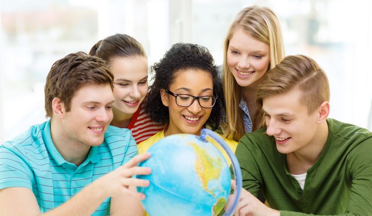 Fünf lächelnde Studierende schauen einen Globus an.