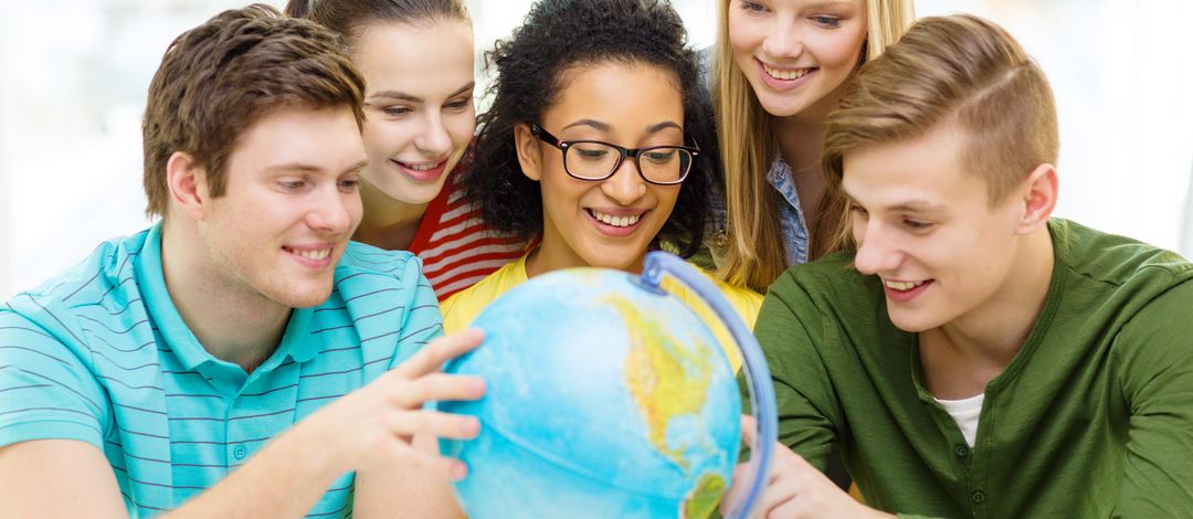 Fünf lächelnde Studierende schauen einen Globus an.