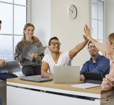 Zu sehen sind eine Gruppe Studierender in einem Seminarraum. Sie freuen sich und machen die "High-Five" Geste.