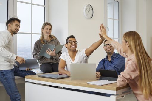 Zu sehen sind eine Gruppe Studierender in einem Seminarraum. Sie freuen sich und machen die "High-Five" Geste.