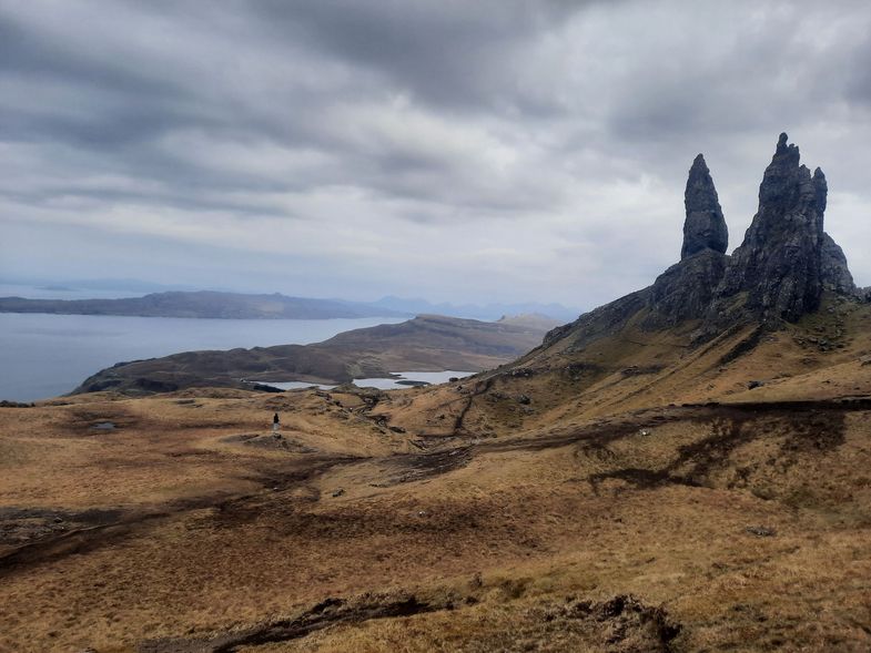 Zu sehen ist die Isle of Skye. Auf der rechten Seite ist der Old Man of Storr. Ein 50 Meter hoher vertikaler Felsen, der befindet sich auf dem Trotternish-Kamm. Man sieht weite moosige Felder und am Horizont Ausläufer von Flüssen und Seen.