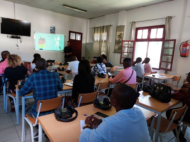 Momentaufnahme eines Unterrichtsgeschehens in Mosambik. Lukas Fiedler steht vor einer Klasse mosambikanischer Studierenden und erklärt etwas am Whiteboard.