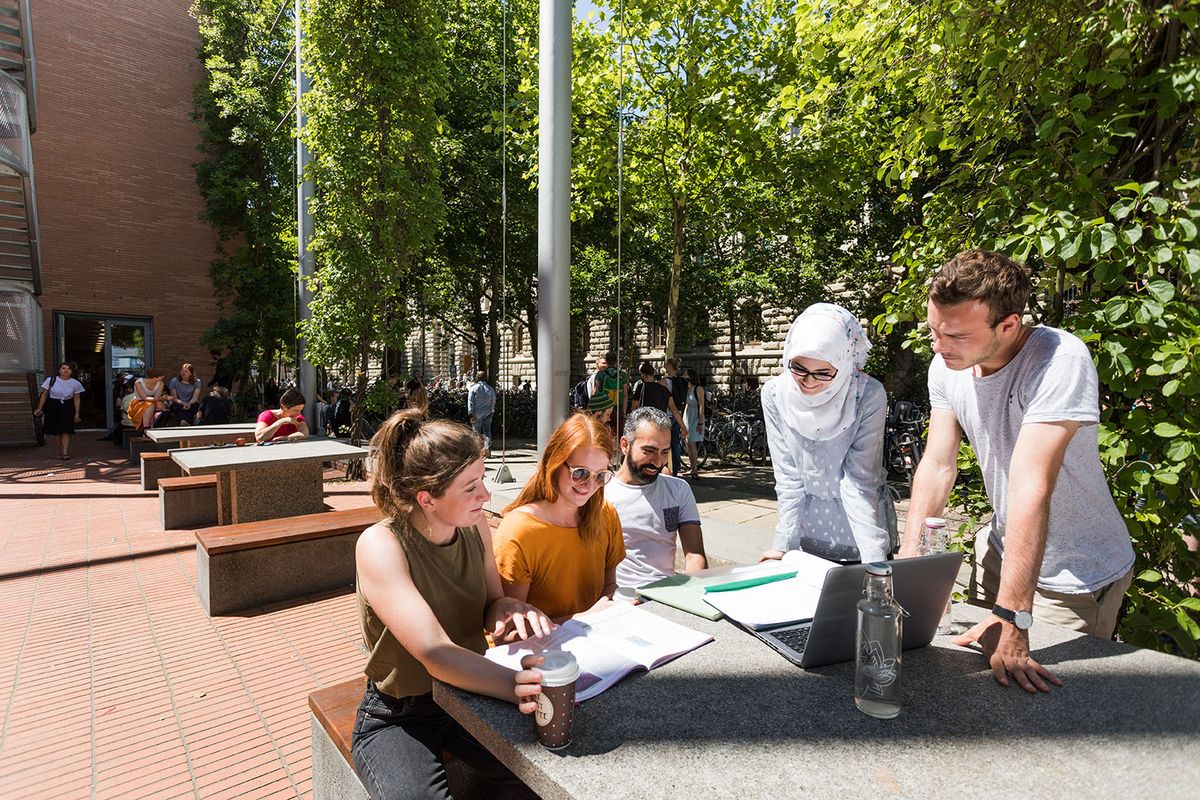 Internationale Studierende lernen auf Tischen und Bänken vor dem Geisteswissenschaftlichen Zentrum.