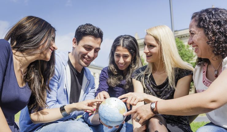 Foto: Eine Gruppe internationaler Studierender betrachtet eine Weltkugel und zeigen sich gegenseitig ihre Heimatländer