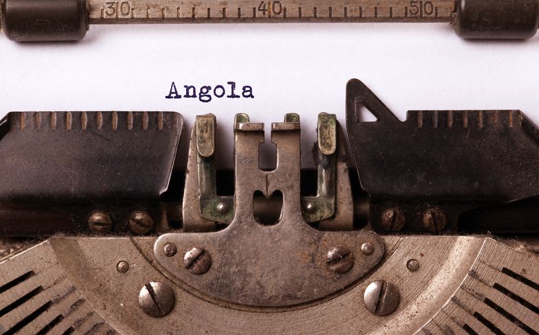 Auf dem Bild ist in Großaufnahme der mittlere Teil einer alten Schreibmaschine zu sehen mit einem eingespannten weißen Blatt, auf dem gerade das Wort "Angola" geschrieben wurde.