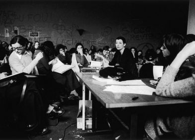 Es handelt sich um ein Schwarz-Weiß-Foto aus den 1970er Jahren. Es wird eine Seminarsituation von ausschließlich weiblichen Studierenden dargestellt. Etwa in der Mitte sitzt eine etwas ältere Frau, die ernst in die Runde schaut, aber viele der anwesenden Studierenden schauen weg oder ziemlich gelangweilt.