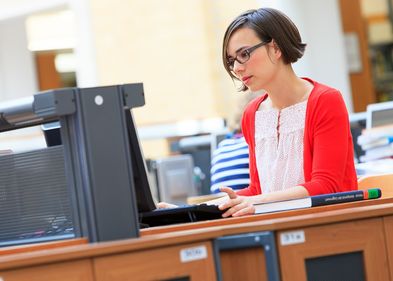 Foto: Eine Junge Frau sitzt in der Universitätsbibliothek am Laptop