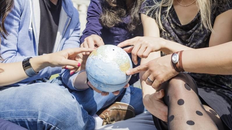 Fünf Jugendliche verschiedener Nationen halten einen kleinen Globus in der Hand.