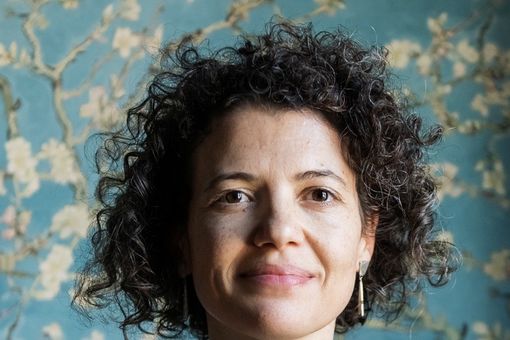 Portraitbild von Dr. Mariana Pinto dos Santos (Lissabon/Portugal) bei Tageslicht vor einer hellblauen Tapete mit weißen Blüten. 