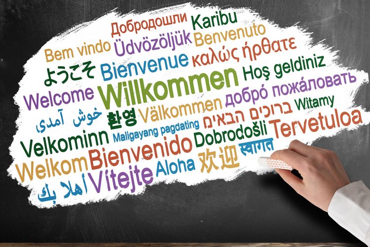 Das Wort Willkommen wird in verschiedenen Sprachen und verschiedenen Farben an eine Tafel geschrieben. Foto: Colourbox