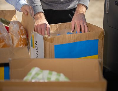 Das Bild zeigt die Hände von Personen, die Spendenboxen für die Ukraine mit Lebensmitteln packen.