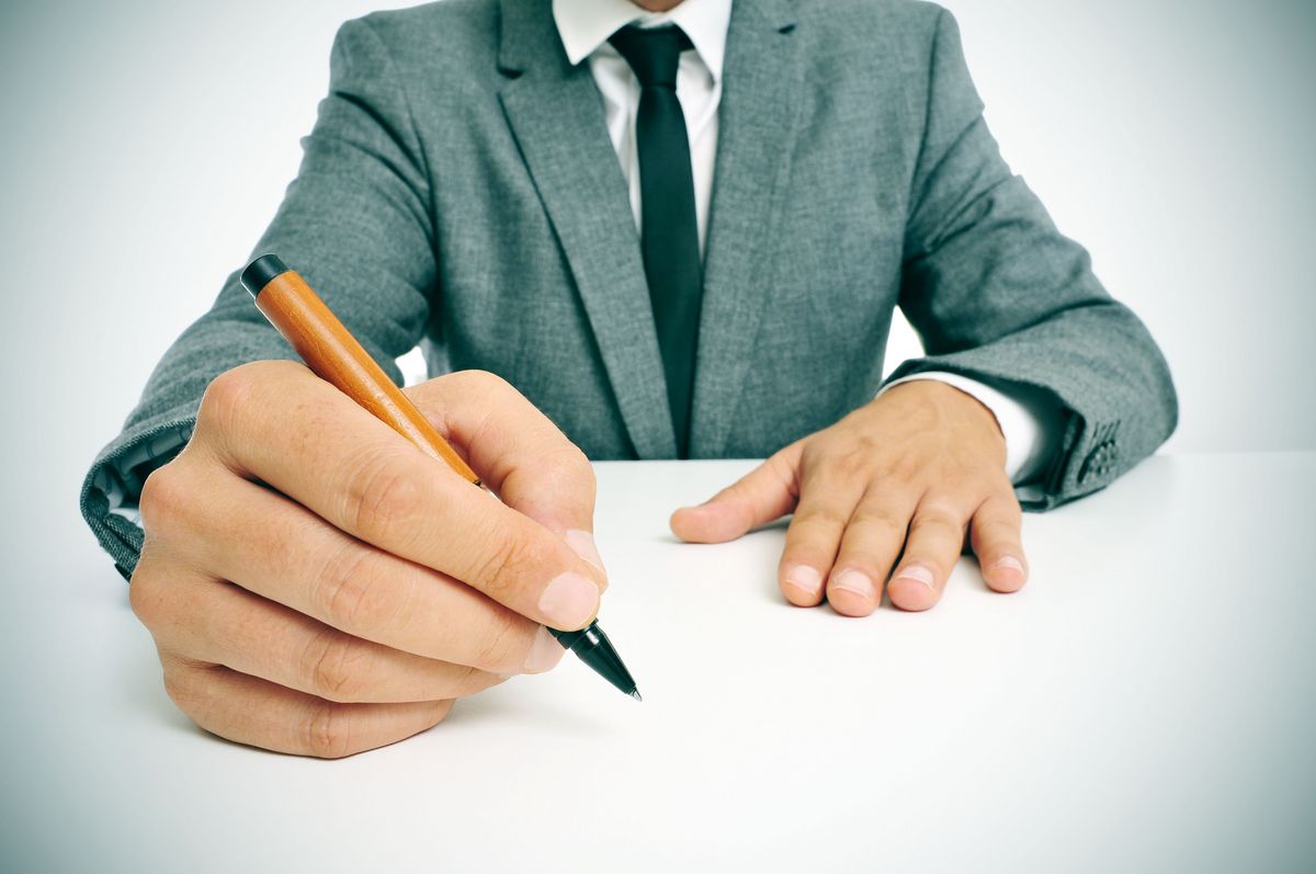 Mann mit Anzug und Krawatte unterschreibt mit organgem Stift bei Tageslicht, Foto: Colourbox