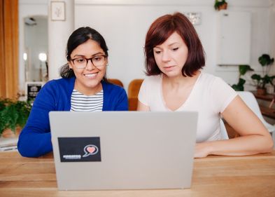 Zwei junge Frauen arbeiten gemeinsam am Laptop.