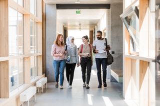 Studierende der Universität Leipzig laufen durch einen Gang des Geisteswissenschaftlichen Zentrums. Das Gebäude ist hell, die Studierenden wirken fröhlich.