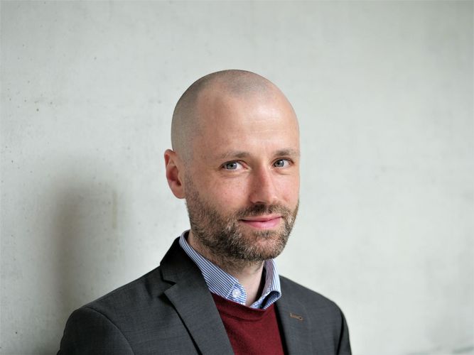 Portraitfoto von Jun.-Prof. Dr. Christian Schmidt bei TAgeslicht vor einer hellgrauen Wand.