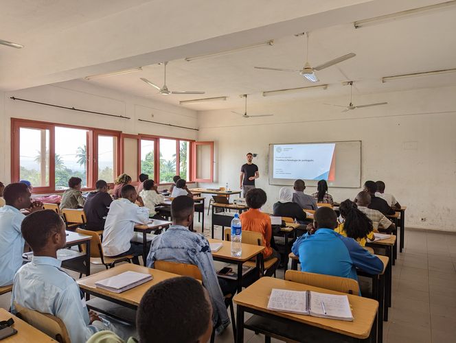Momentaufnahme eines Unterrichtsgeschehens in Mosambik. Lukas Fiedler steht vor einer Klasse mosambikanischer Studierenden und erklärt etwas am Whiteboard.