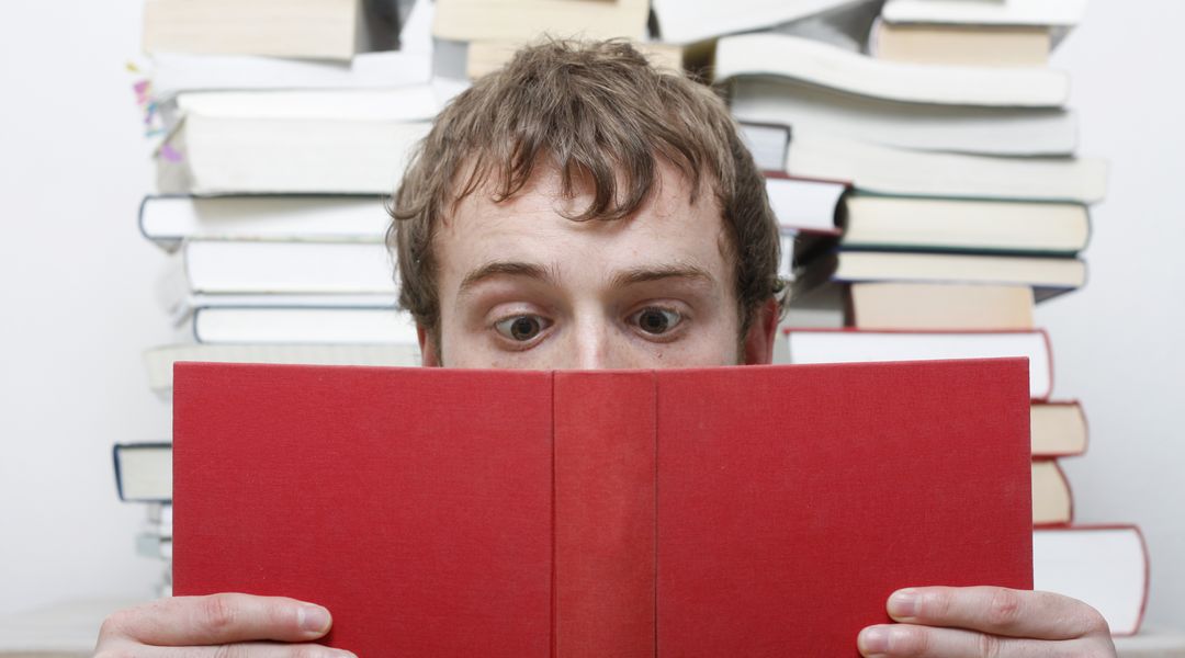 Das Bild zeigt einen jungen Mann, der in einem Buch liest und dabei die Augen verdreht. Foto: Colourbox