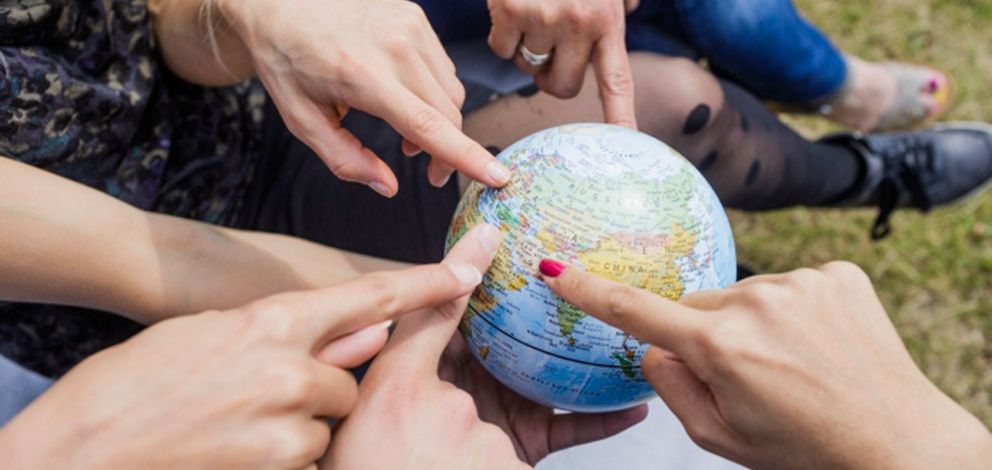 Foto: verschiedene Hände zeigen auf eine kleine Globuskugel