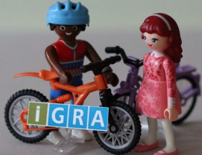 two Playmobil figures with bicycles, in the foreground is the IGRA logo