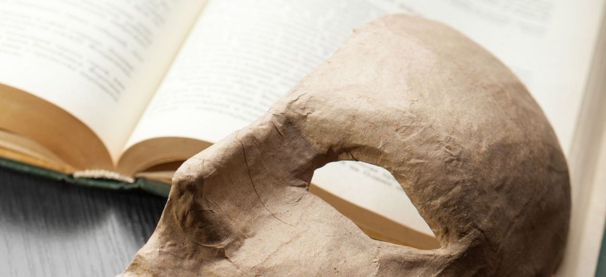 dekoratives Bild einer Maske, die auf einem aufgeschlagenem Buch liegt