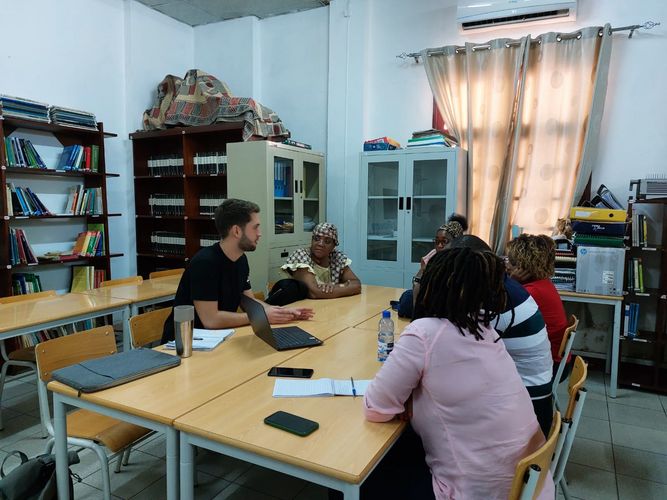 Lukas Fiedler sitzt mit einigen mosambikanischen Studierenden um eine Tischgruppe und erklärt etwas.