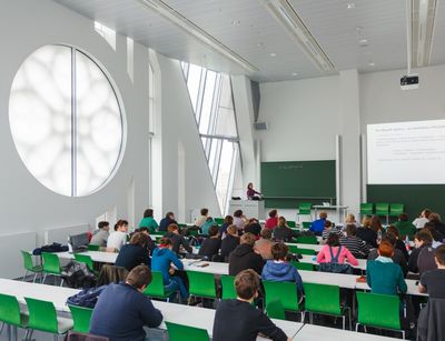 Foto: Studierende während einer Vorlesung in einem Hörssal mit grünen Stühlen