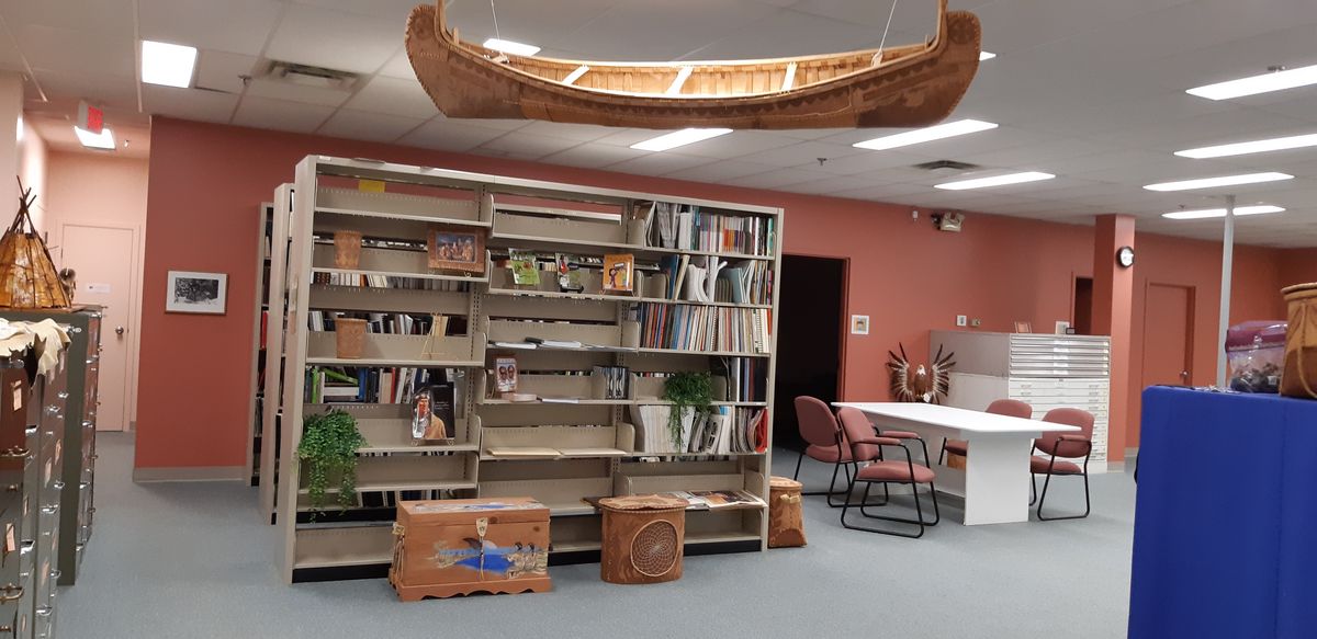 zur Vergrößerungsansicht des Bildes: Das Bild zeigt Bücherregale und traditionelles Kunsthandwerk im Lesesaal des Nationalarchivs der Atikamekw in Kanada