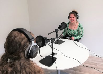 Zwei Studentinnen mit Mikrofonen und Kopfhörern nehmen einen Podcast auf. 